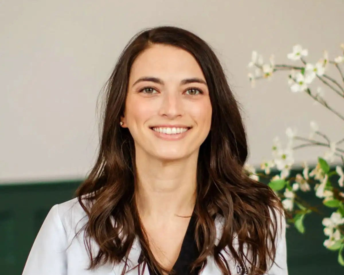 Woman in a white coat standing indoors with a neutral background